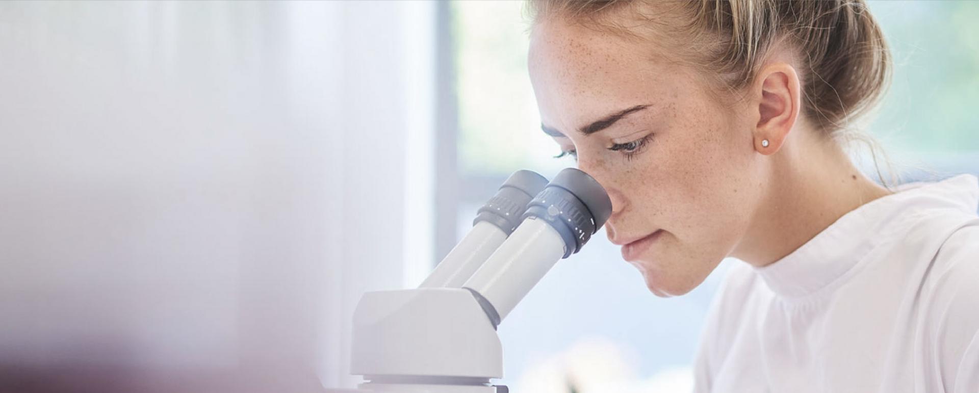 kvinnelig student som ser inn i et mikroskop