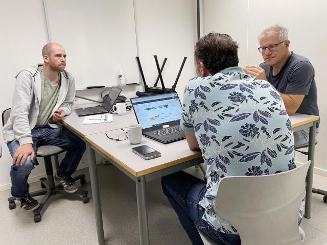 Tre menn sitter i diskusjon i klasserom foran en pc-skjerm